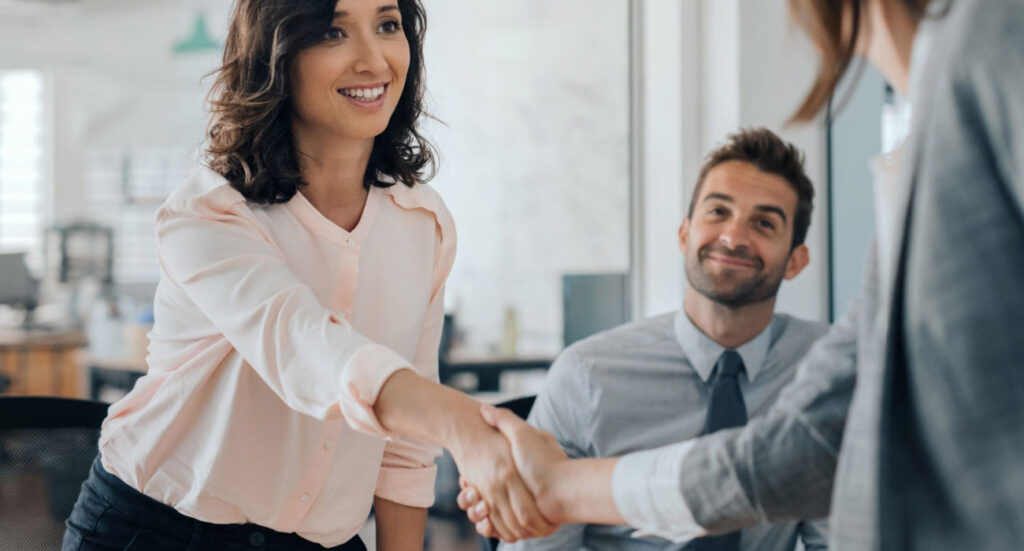 Business professionals shaking hands in an office, symbolizing teamwork, trust, and collaboration in coaching.