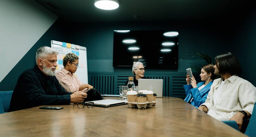 Business team engaged in large group facilitation workshop with laptops, whiteboard, and discussion.