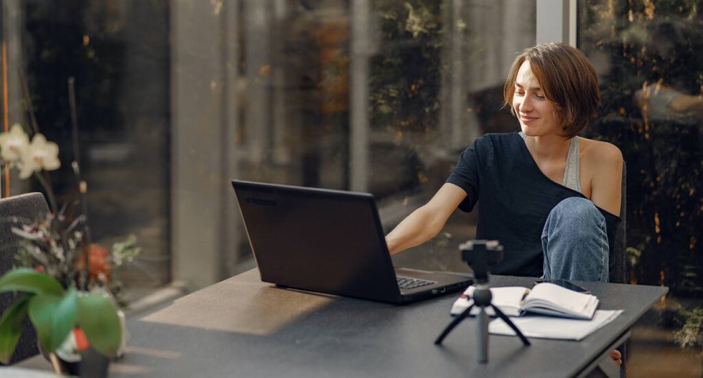 Young professional engaging in online leadership development session with laptop, notebook, and camera setup.