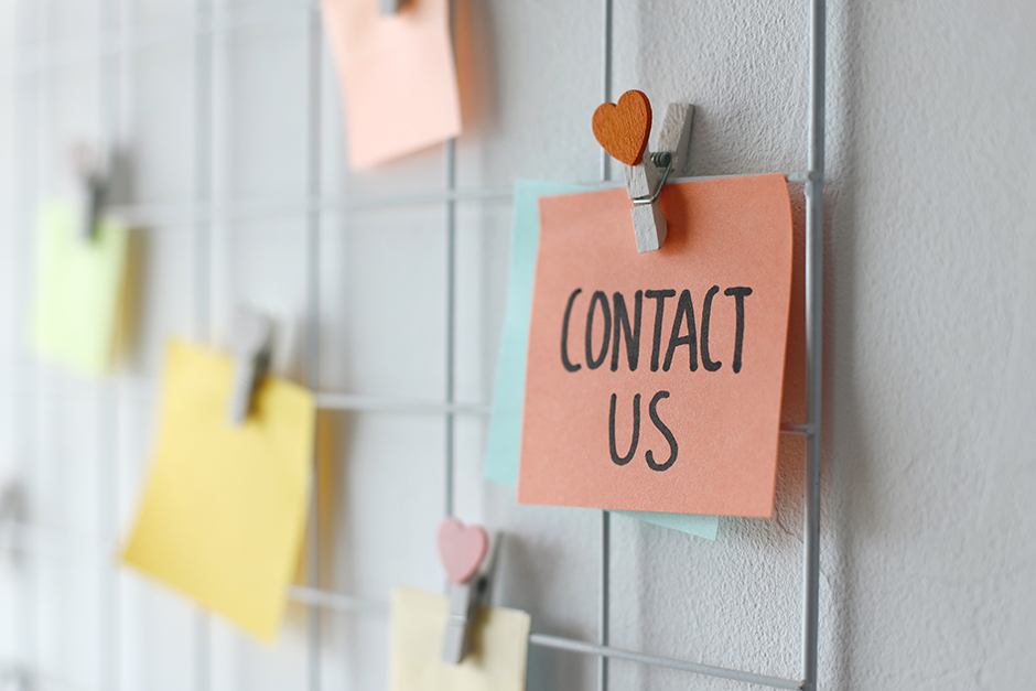 Sticky note reading "Contact Us" clipped to a wire board with colorful notes